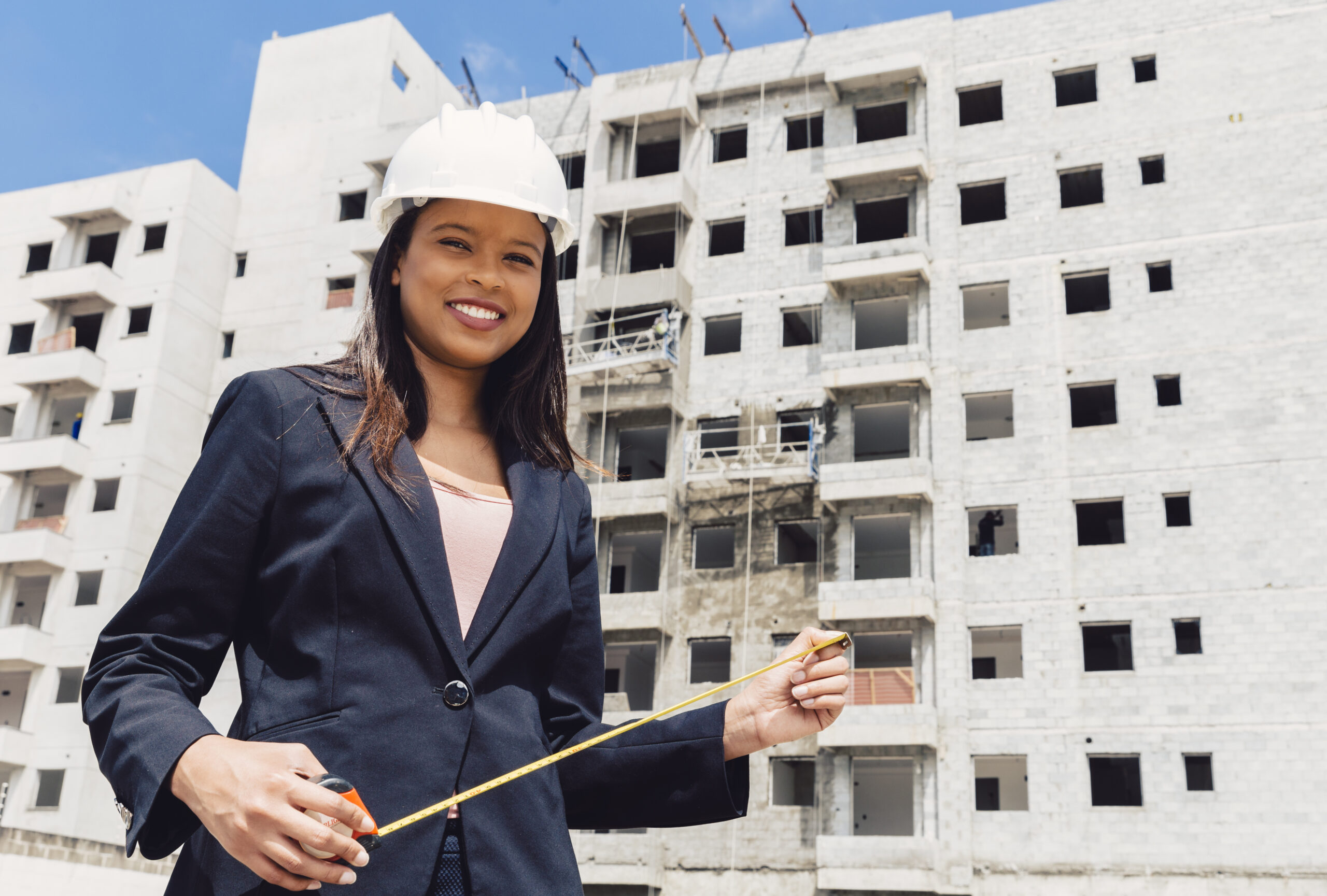 happy-african-american-lady-safety-helmet-with-measuring-tape-near-building-construction